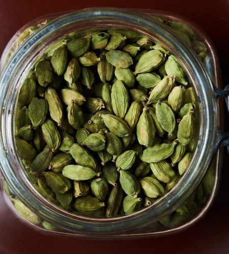 Closeup proto of glass jar full of green cardamom pods on brown plate. Top view.