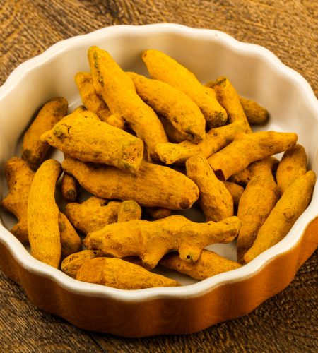 Tumeric roots heap in the bowl over wooden background